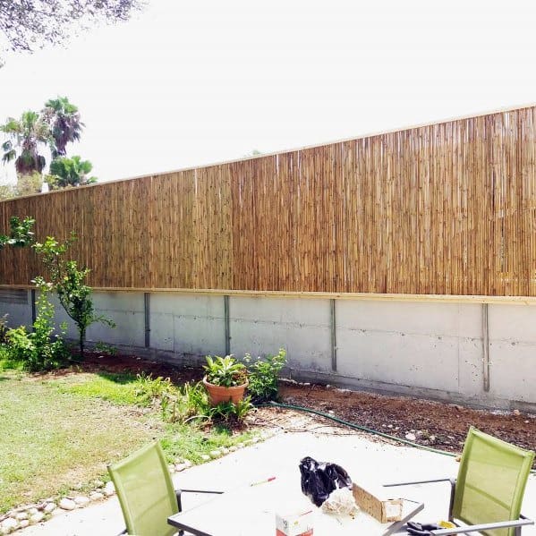Bamboo privacy fence built on a concrete base in a sunny backyard with patio furniture.