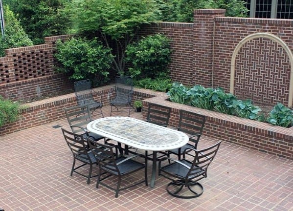 Outdoor patio with brick walls, a table, and chairs enveloped in lush greenery