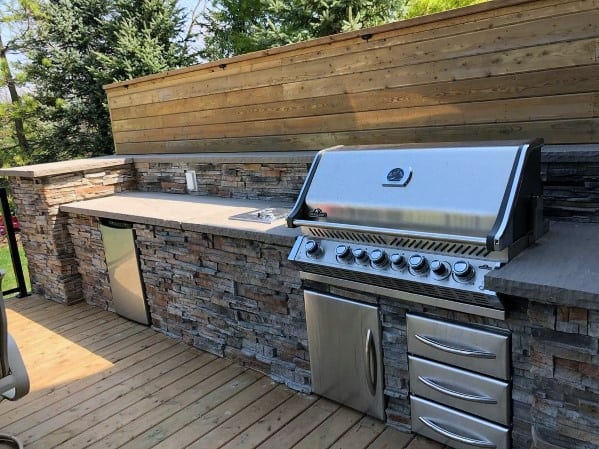 Outdoor kitchen with a built-in stainless steel grill, stone countertops, and wood deck flooring