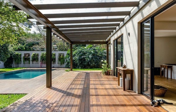 Pergola with a transparent roof, wooden deck, and poolside view extending from the house.