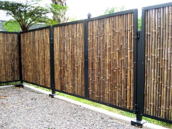 Metal-framed bamboo fence with vertical bamboo panels surrounding a gravel yard in a modern tropical landscape.