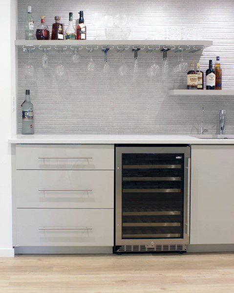 Stylish home bar with a white textured stone backsplash, glass racks, sleek cabinetry, and a built-in wine cooler