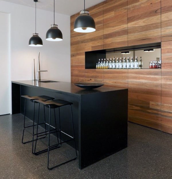 Modern kitchen with a black island, wooden wall, and bar shelves, highlighted by three pendant lights hanging above