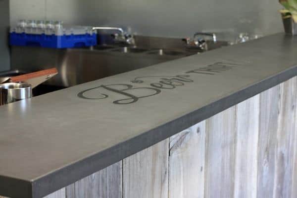 Concrete bar top with engraved text and rustic wooden base in a modern home bar setup.