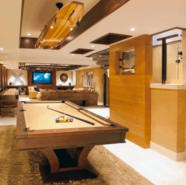 Luxury basement billiard room with tan pool table, warm wood accents, and cozy lounge area.