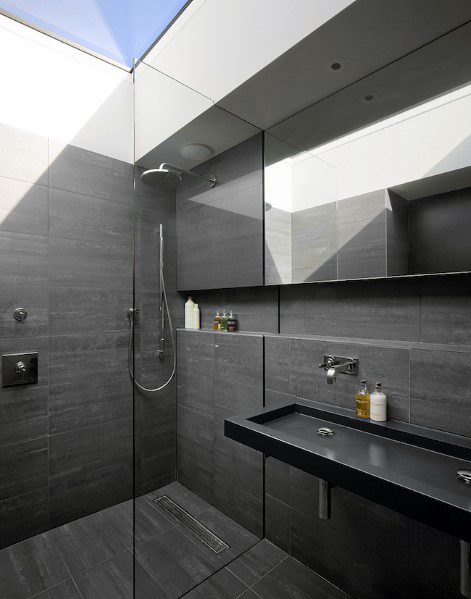 Sleek black bathroom with glass shower, wall-mounted faucet, and natural skylight.