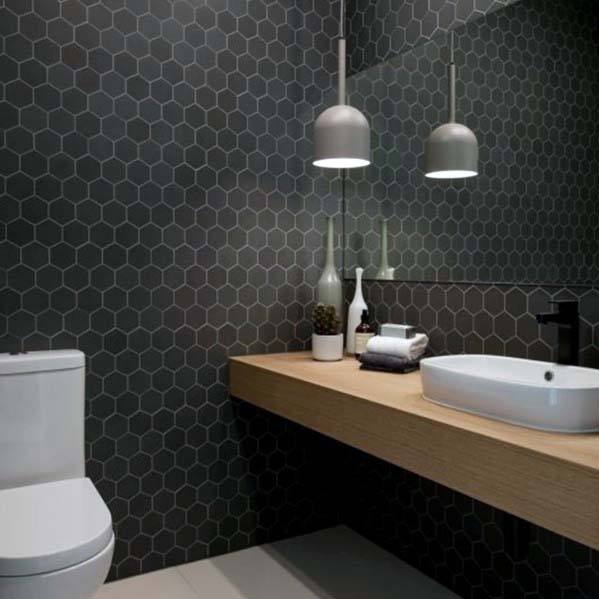 Contemporary black bathroom with hexagonal tiles, wooden vanity, and pendant lighting.