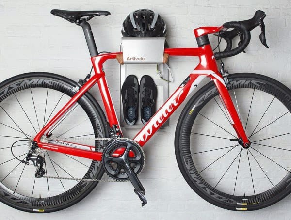 Wall-mounted bike rack with an integrated shelf for helmet and shoes, combining functionality and style for indoor bicycle storage.