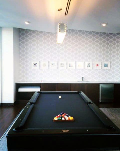 Minimalist billiard room with black felt table, patterned wallpaper, and modern lighting.