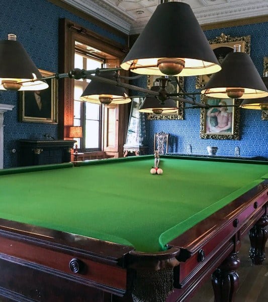 Vintage-style billiard room with blue walls, framed art, and classic overhead lighting.