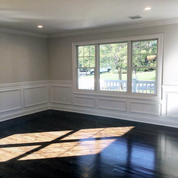 Spacious room with white chair rail molding, large windows, and dark hardwood floors illuminated by natural light