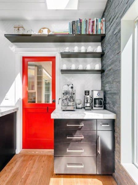 Modern coffee bar with dark cabinets, red door, floating shelves, and coffee machines.