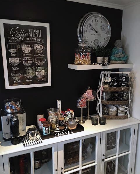 Stylish coffee bar with black wall, framed menu, glass cabinets, clock, and decorative accents.