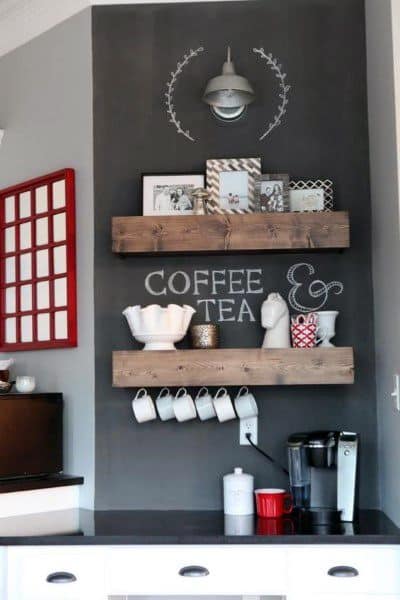 Compact coffee bar with dark wall, wooden shelves, mugs, decor, and a coffee machine.