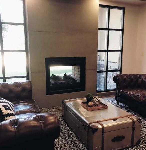 Cozy living room featuring a concrete fireplace paired with vintage leather sofas and industrial-style windows.