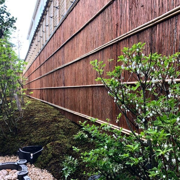 Rust-colored bamboo privacy fence with horizontal bamboo framing, surrounded by lush greenery.