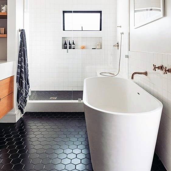 Modern bathroom with black hexagon floor tiles, white freestanding tub, and glass shower.