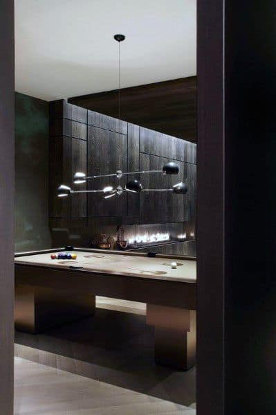Minimalist billiard room with dark wood paneling, beige pool table, and modern pendant lighting.