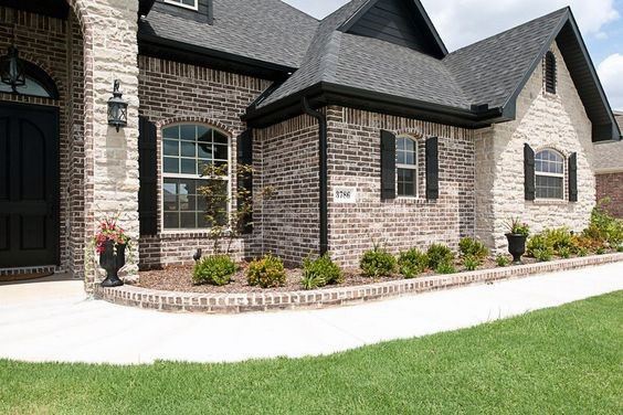 Charming home with dark brick and light stone cladding, black shutters, arched windows, and a landscaped walkway for a cozy curb appeal