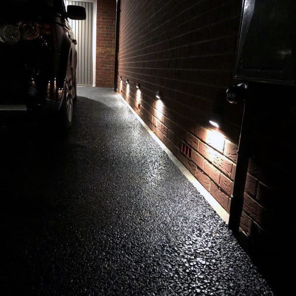 Driveway path illuminated by sleek wall-mounted lights along the brick wall, creating a clean and modern look at night