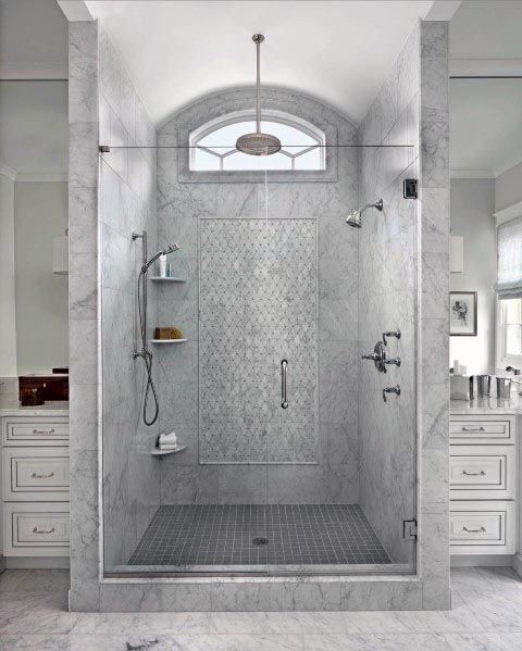 A luxurious gray bathroom with a marble walk-in shower, glass enclosure, mosaic details, and natural lighting.