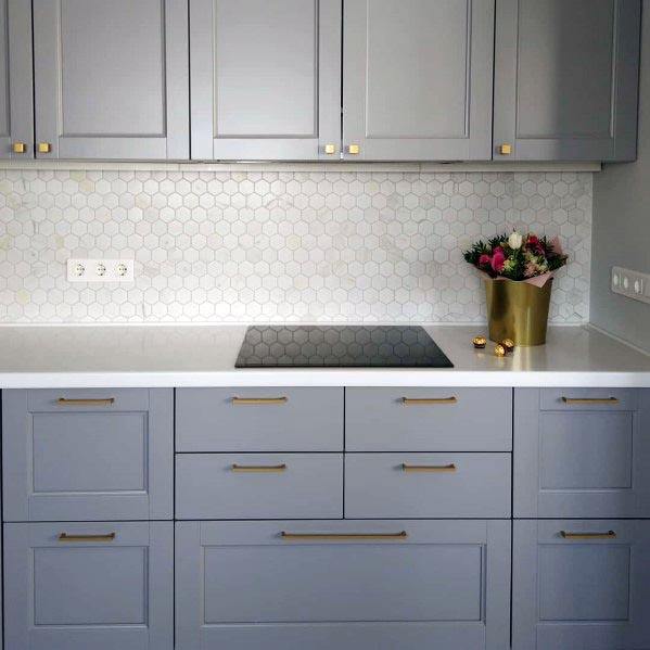 Light grey kitchen cabinets with gold handles, white hexagon backsplash, and induction cooktop.