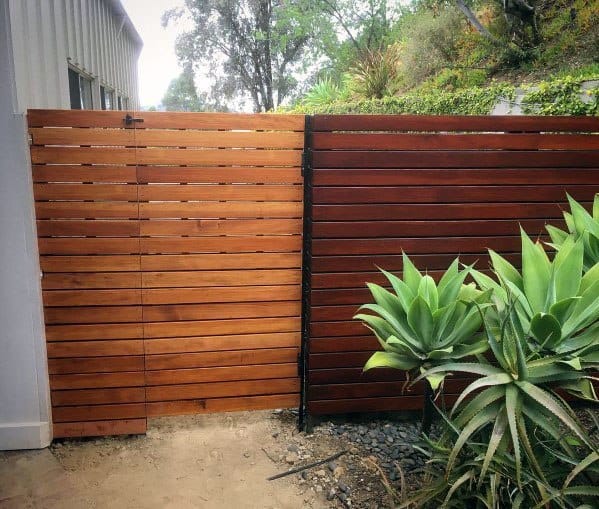 Wooden fence with a gate next to green succulents and plants in a garden setting