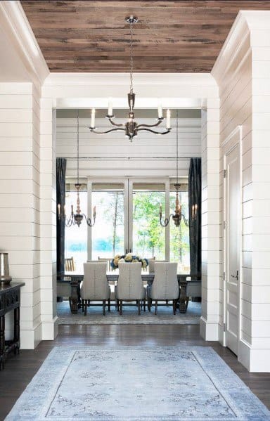 Bright foyer with wood plank ceiling, shiplap walls, chandelier, and view of dining area.
