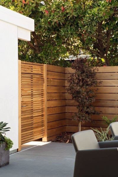 A wooden privacy fence and gate surrounded by greenery in a modern patio setting