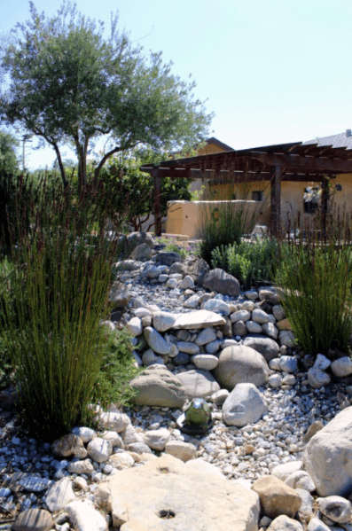 Natural river rock landscaping with large stones, plants, and a pergola, creating a peaceful outdoor setting with a desert-inspired look