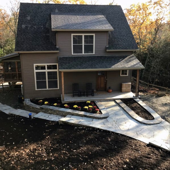 A stone-bordered walkway leading to a house, surrounded by colorful flowers and freshly mulched garden beds