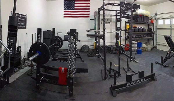 Garage gym with bench press, power rack, chains, weight storage, and American flag decor.