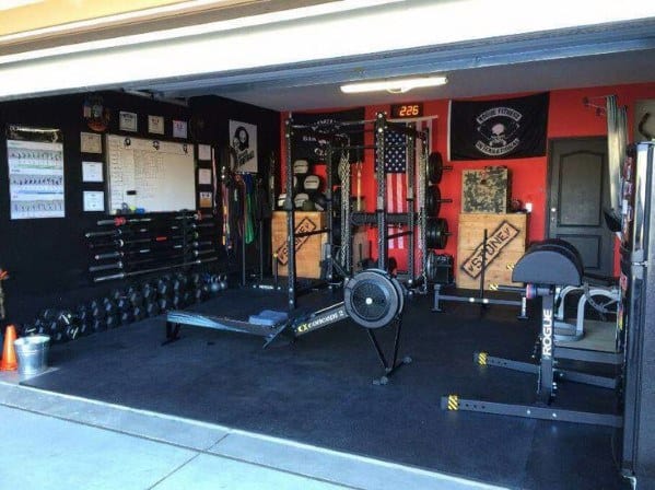 Garage gym with rowing machine, weight racks, barbell storage, and motivational wall decor.