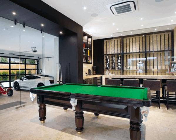 Modern billiard room with green felt table, bar area, and glass doors to a luxury garage.