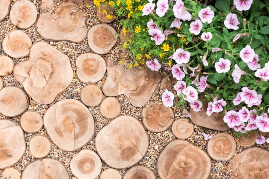 Wooden log slices with pink and white flowers on a gravel walkway