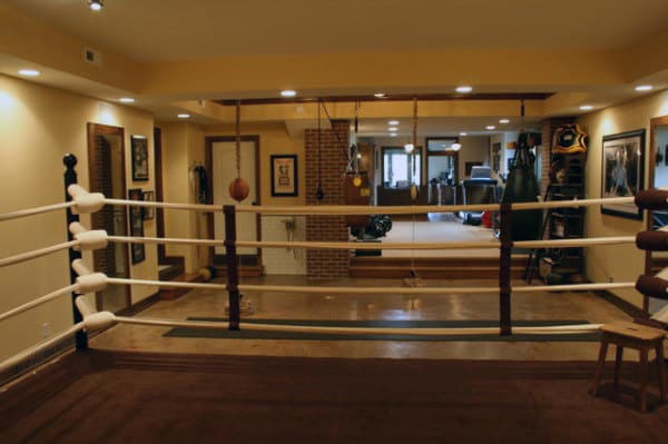 A cozy home gym with a boxing ring, punching bags, and equipment in a well-lit basement space
