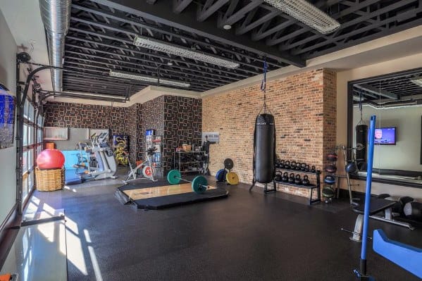 Spacious home gym with brick walls, rubber flooring, punching bag, weightlifting platform, and cardio equipment.