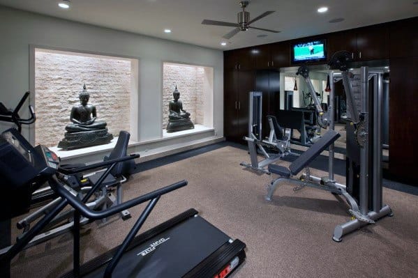 Home gym with Buddha statues, treadmill, strength machines, and warm ambient lighting.