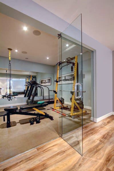 Home gym with glass door, wooden flooring, wall mirrors, and yellow workout equipment.
