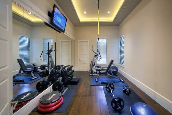 Home gym with hardwood floors, wall mirrors, TRX system, cardio equipment, and free weights.