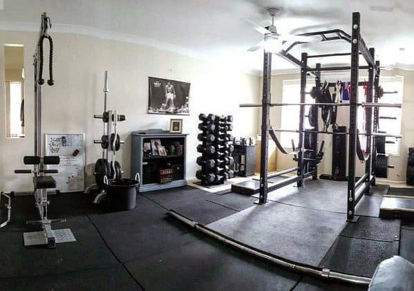 Home gym with rubber flooring, power rack, dumbbells, and various strength training equipment.
