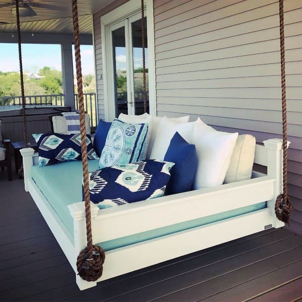 Porch hanging daybed with nautical-themed cushions, rope supports, and a relaxing outdoor vibe.