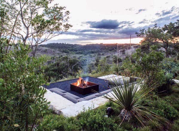 Cozy outdoor fire pit surrounded by greenery, overlooking a scenic valley at sunset