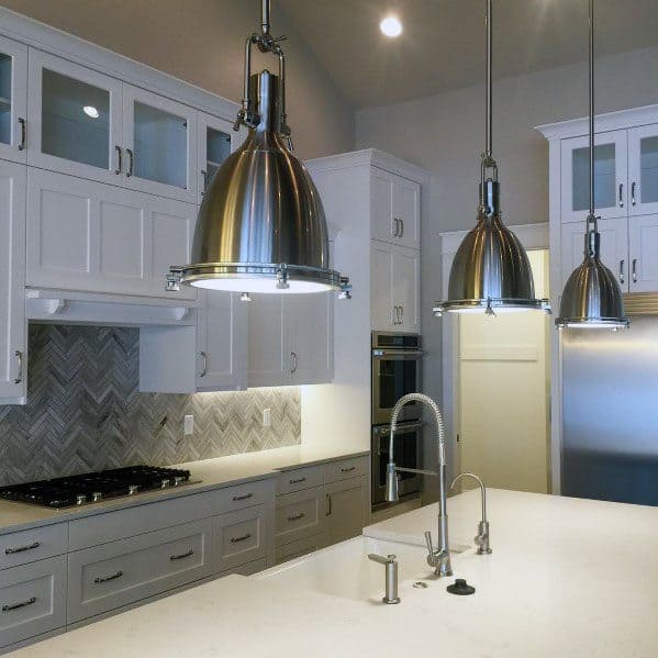 Modern kitchen with a grey herringbone stone backsplash, white cabinets, industrial pendant lights, and a large island