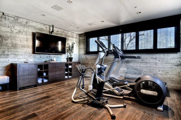 Home gym with rustic wood walls, hardwood flooring, cardio equipment, and a wall-mounted TV.