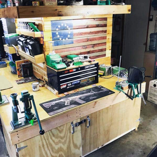 Patriotic-themed reloading bench with wooden cabinetry, organized tools, and a decorative American flag backdrop