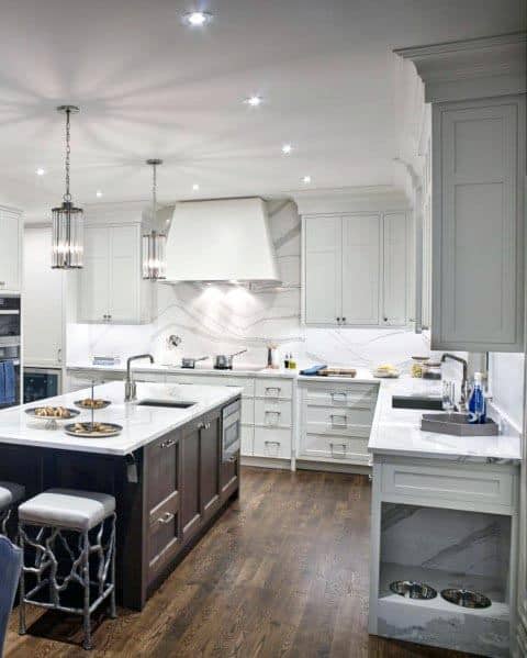 White kitchen with dark wood island, marble countertops, pendant lighting, and hardwood floors.