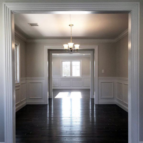 Spacious interior with white chair rail molding, dark hardwood floors, and a central chandelier for a refined and elegant atmosphere