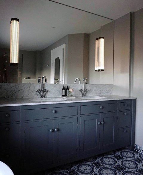 Bathroom with marble countertop, dark cabinetry, and tall ribbed linear wall sconces.