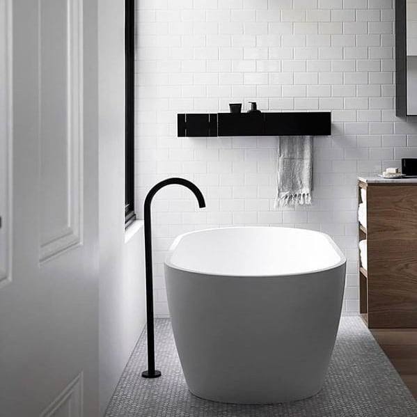 Minimalist bathroom with freestanding tub, white subway tile wall, and black fixtures.